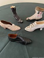 Five miniature decorative Victorian-style shoes arranged on dark fabric, showcasing varying designs and embellishments.
