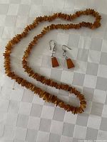 Amber necklace and earrings laid on a white textured fabric surface showing the overall set.