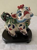 Front angled view of colorful Asian ceramic pig figurine with detailed painted designs on its body and face, mounted on a wooden stand.