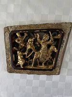 Front view of the trapezoidal wooden carving showing gold leaf accented figures and horse in a relief design.