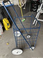 Blue metal wire folding buggy with large white wheels sitting on concrete floor