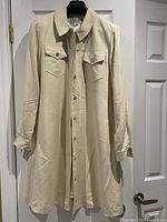 Cream-colored Evan-Picone long silk lined coat with front buttons, shirt collar, flap chest pockets, and long sleeves with button cuffs.