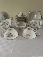 Multiple Mikasa Fine China tea or coffee cups and saucers displayed, showing white porcelain with gray leaf pattern and silver-tone trim.