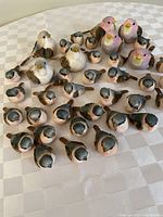 Photo displaying group of ceramic or resin bird figures varying in color and size including pink, white, and apricot with a textured finish.