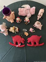 Collection of pig-themed items laid out including plush pig pouch, ceramic pig mug, pig figurines, and red pig shaped Christmas hangings on a black surface.