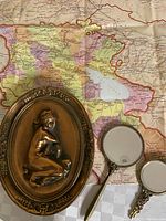 Two small handheld purse mirrors with ornate metal handles and backs placed next to the wall decor