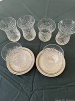 Six clear cut crystal Turkish tea cups arranged in two rows with some placed on silver-like saucers, all on a dark green tablecloth.