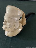 Close view of the carved meerschaum pipe showing the man's head with detailed hat and tassel, and visible repair on the hat.