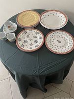Full lot with 3 black and white patterned plates, 3 yellow cane patterned plates, 3 espresso cups with saucers, and 2 bowls arranged on a round table.
