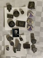 Overview of 17 metal pins of different shapes and designs, all featuring Armenian writing or images