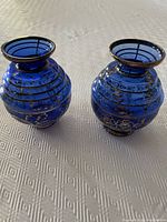 Two cobalt blue glass vases side by side showing the silver overlay designs and round bodies with narrow necks.