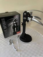Photo showing new wine bottle opener with black base and two silver lever handles next to the original product box and foil cutter accessory.