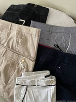 Photo showing six pairs of women's pants folded and stacked, displaying various colors and fabric textures.