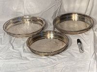 Three silver plated trays of different sizes photographed on fabric background with marker for scale.