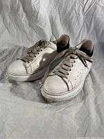 Front angle showing white leather sneakers with scuffed surfaces and worn laces on white fabric background.