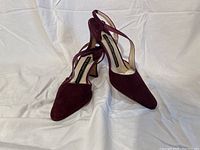 Pair of wine colored suede pumps positioned together on a white backdrop, showing the front and straps.