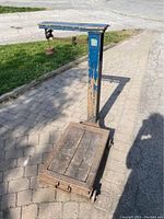 Full view of an antique grain weigher showing a metal frame painted blue, with worn paint and a wooden platform base.