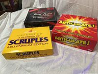 Lot of three board games: Trivial Pursuit 10th Anniversary, Articulate!, and A Question of Scruples Millennium Edition. All boxes visible for identification.