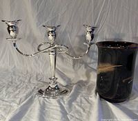 Silver plated 3-candle candelabra and handmade pottery vase on white fabric background.