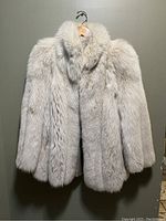 Front view of the vintage fox fur coat hanging on a hanger showing dense natural fox fur in a light cream color with a full fur collar.