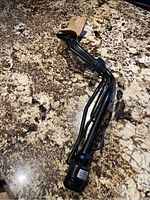 Full view of the black metal fuel tank filler neck tube placed on granite countertop, showing the curved shape and three pipe lines.