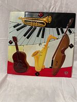 Front view of square glass art piece with colorful 3D musical instruments including trumpet, piano keys, violin, saxophone, and guitar.