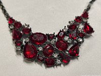 Close-up showing the cluster arrangement of various shapes of red cubic zirconia and small clear cubic zirconias set in dark metal.