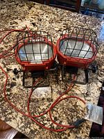 Two red Husky work lights with protective cages and cords, placed on a granite countertop.