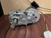 Side view showing the metallic gearbox with splined shaft and attached electric motor with wiring and connector