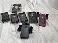 Six OtterBox iPhone cases laid out with their holster belt clips on a white fabric surface.
