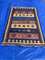 Top view of rectangular Kilim style rug on blue tarp showing geometric diamond pattern and colorful border.