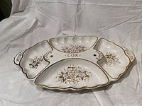 Full view of white ceramic divided platter with gold trim and labeled sections for lox, bagels, cheese, and butter with floral decoration in each section.