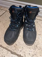 Front view of black winter boots with blue laces and Cloudveil logo on tongue.