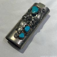 Front view of the silver lighter cover showing turquoise stone decoration and embossed leaves and vine swirls.