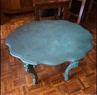 Top view of the antique table showing the scalloped edges, flat painted surface, and its size relative to nearby furniture.