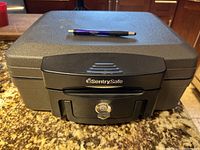 Front view of a black SentrySafe fireproof safe on granite countertop with a pen on top for scale.