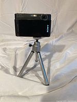 Sony DSC-T90 camera mounted on tripod showing front lens side with Carl Zeiss lens label.