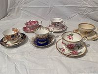 Six vintage teacup and saucer sets arranged on white fabric background