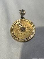 Front view of the round gold-tone zodiac pendant showing all zodiac signs with a star in the center and a clasp at the top.