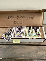 Box filled with approximately 500 1984 O-Pee-Chee hockey cards, showing the front part of many cards laid out revealing player images and the box lid labeled with the year and brand.