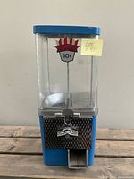 Front view of the Advance A-105 candy dispenser vending machine showing blue metal base, clear plastic candy container, and coin slot mechanism with Advance 10 cent logo.