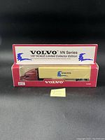 Two photos of boxed Volvo VN Series 1/87 scale die cast metal collectible trucks with maroon cabs and beige Volvo branded trailers.