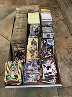 Photo showing a large assortment of sports cards in various stacks inside a long box, including sleeved cards and loose cards.
