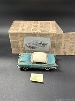 Image of the blue and white 1957 Chevy Bel Air resin sculpture in front of its original box with vintage newspaper print and sketch of the car.