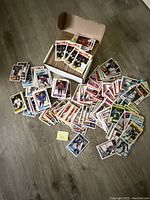 Overview of loose 1980s hockey cards spread on floor near a box.
