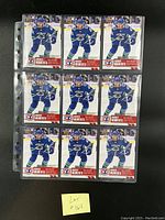 Front view of nine Quinn Hughes rookie cards in a protective sleeve, showing the player in blue Vancouver Canucks uniform with 'Rookie Moments' label.