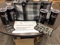 Photo showing Thirty One black plaid carrier bag, 4 insulated tumblers with black lids branded ALSC, black and white canvas wallet with abstract design, black and white patterned flip flops, and two LCBO gift cards on table.