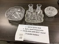 Photo of three glass candy dishes including shell-shaped, square scalloped, and round with lid, plus two small candle holders spread on table with size info card
