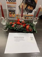 Front view of entire holiday centrepiece showing glass candle holder, two glass angels, red taper candles, and holly decoration.