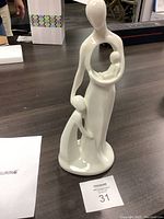 Full view of the white glazed ceramic figurine showing the mother holding an infant with a standing child.
